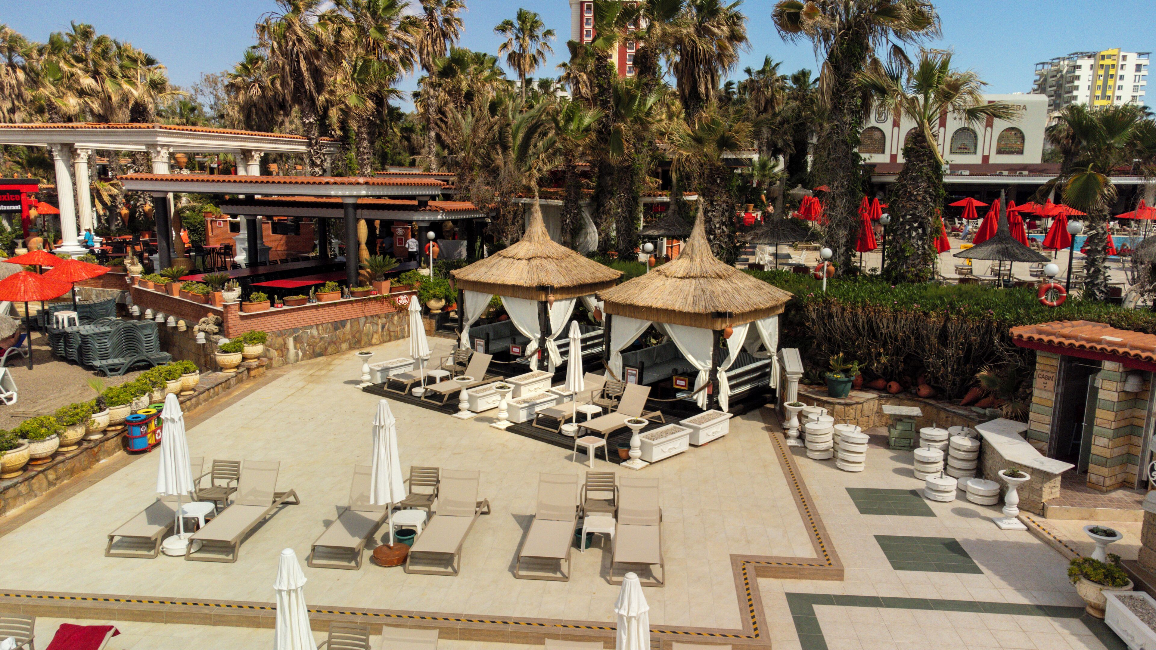 A resort with outdoor seating areas, palm trees, and a thatched-roof gazebo.