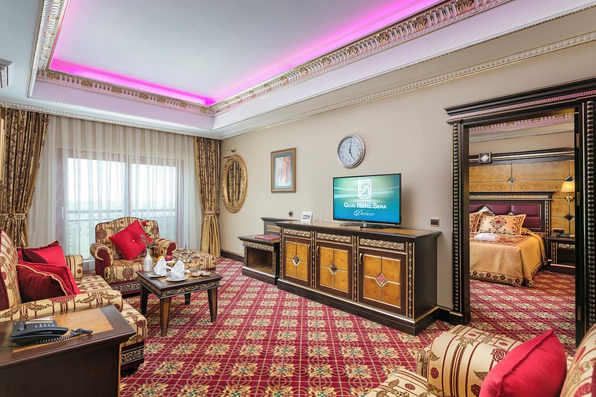 A hotel room with a red carpet, a sofa set, a television, and a bed with a headboard.