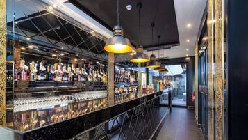 A bar area with a polished black countertop, multiple hanging pendant lights, and shelves stocked with bottles and glasses.