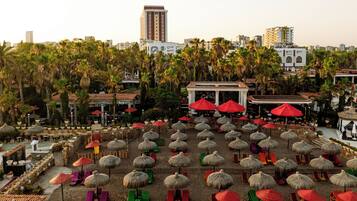 A beachside resort with thatched umbrellas, lounge chairs, and a view of the city skyline.