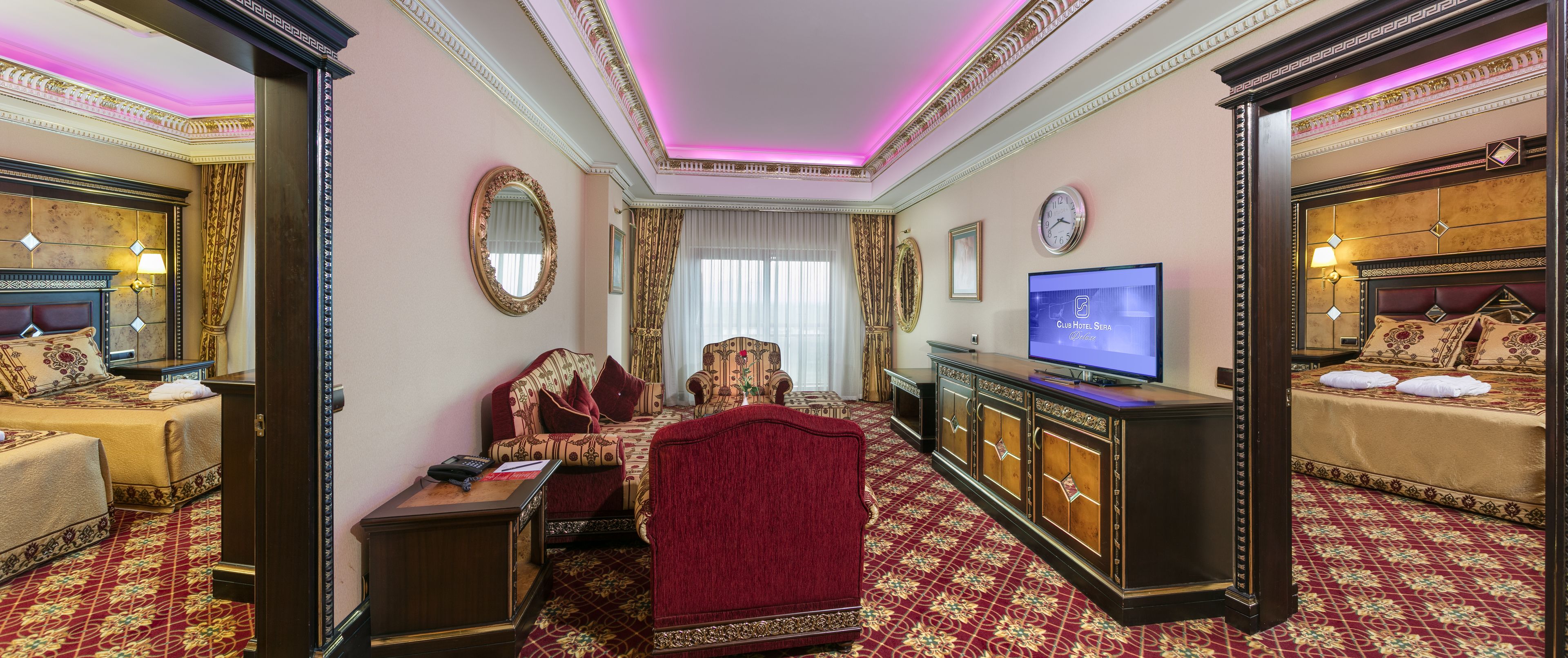 A luxurious hotel room with a large bed, a sitting area with a red sofa, a television, and ornate decor.
