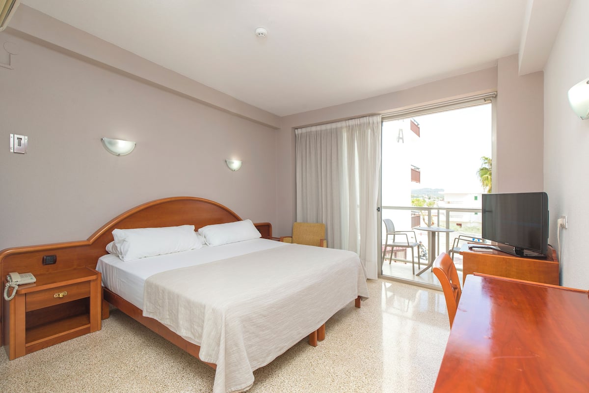 A hotel room with a bed, bedside table with a phone, a TV, a chair, and a balcony with a view.