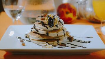 Una pila de tortitas con salsa de chocolate y nueces sobre un plato blanco.