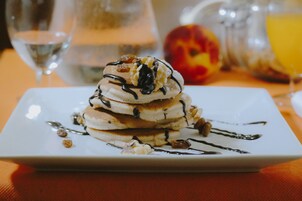 Una pila de tortitas con salsa de chocolate y nueces sobre un plato blanco.