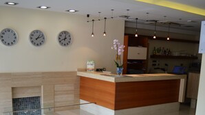 A modern hotel lobby with a reception desk, a seating area with a sofa and a coffee table, and a kitchen in the background. - Hotel Marfil (Sant Antoni de Portmany)
