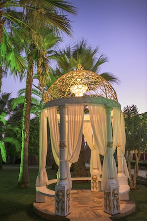 A gazebo with a dome and draped curtains, surrounded by palm trees.