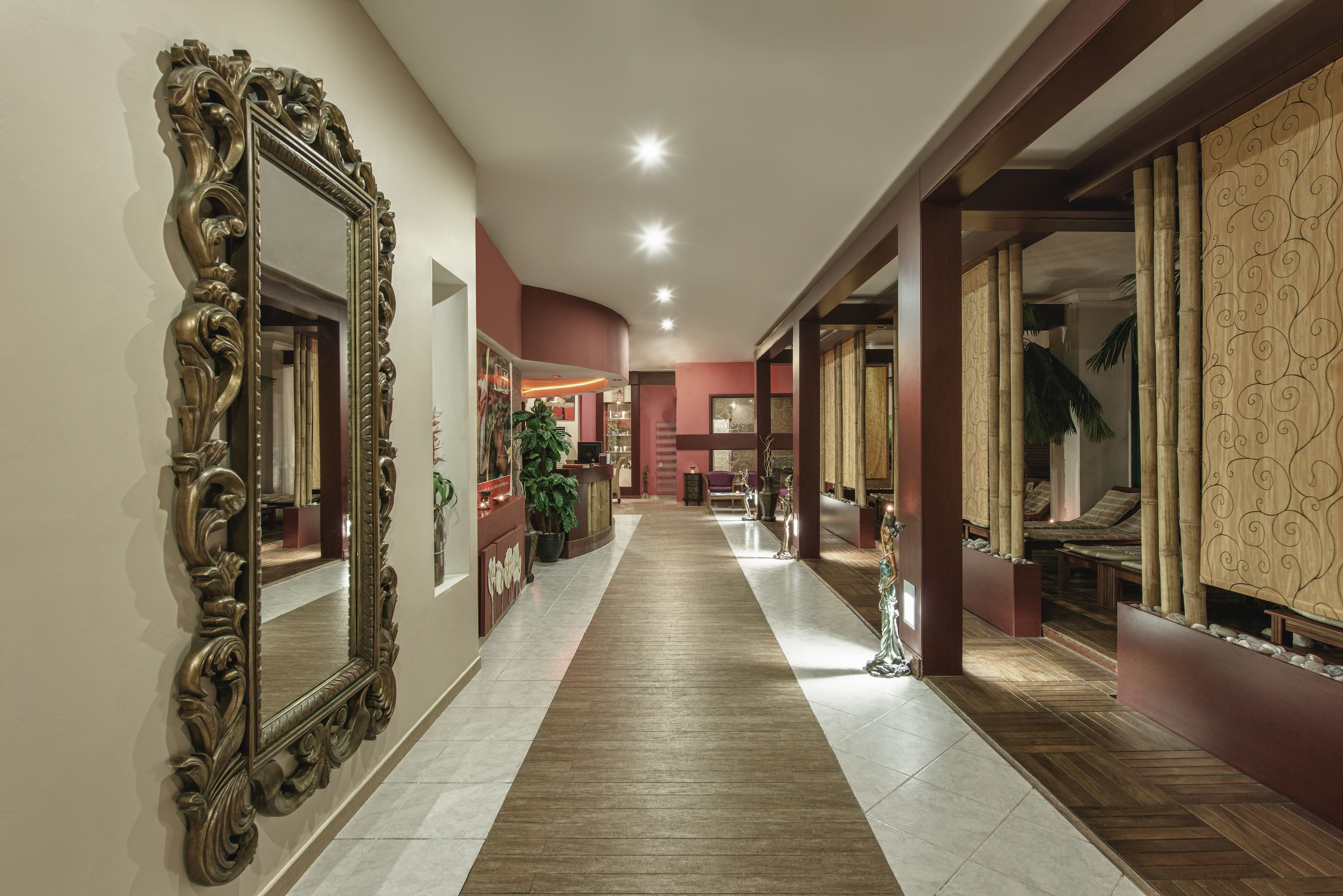 A hallway with a large ornate mirror, a wooden floor, and a red wall.