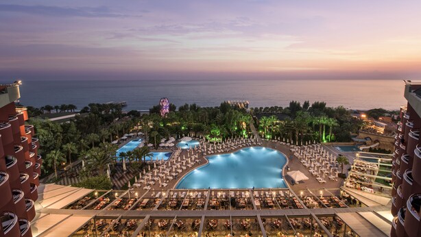 A resort with a large pool, multiple smaller pools, and a view of the ocean at sunset.