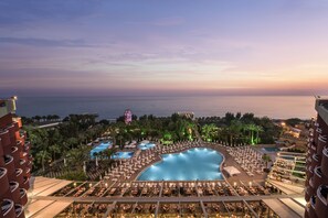 A resort with a large pool, multiple smaller pools, and a view of the ocean at sunset. - Delphin Deluxe Resort Hotel - All Inclusive (Alanya)