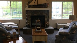 A cozy living room with a stone fireplace, comfortable seating, and large windows offering a view of the outdoors. - South Beach Resort Hotel (Marblehead)