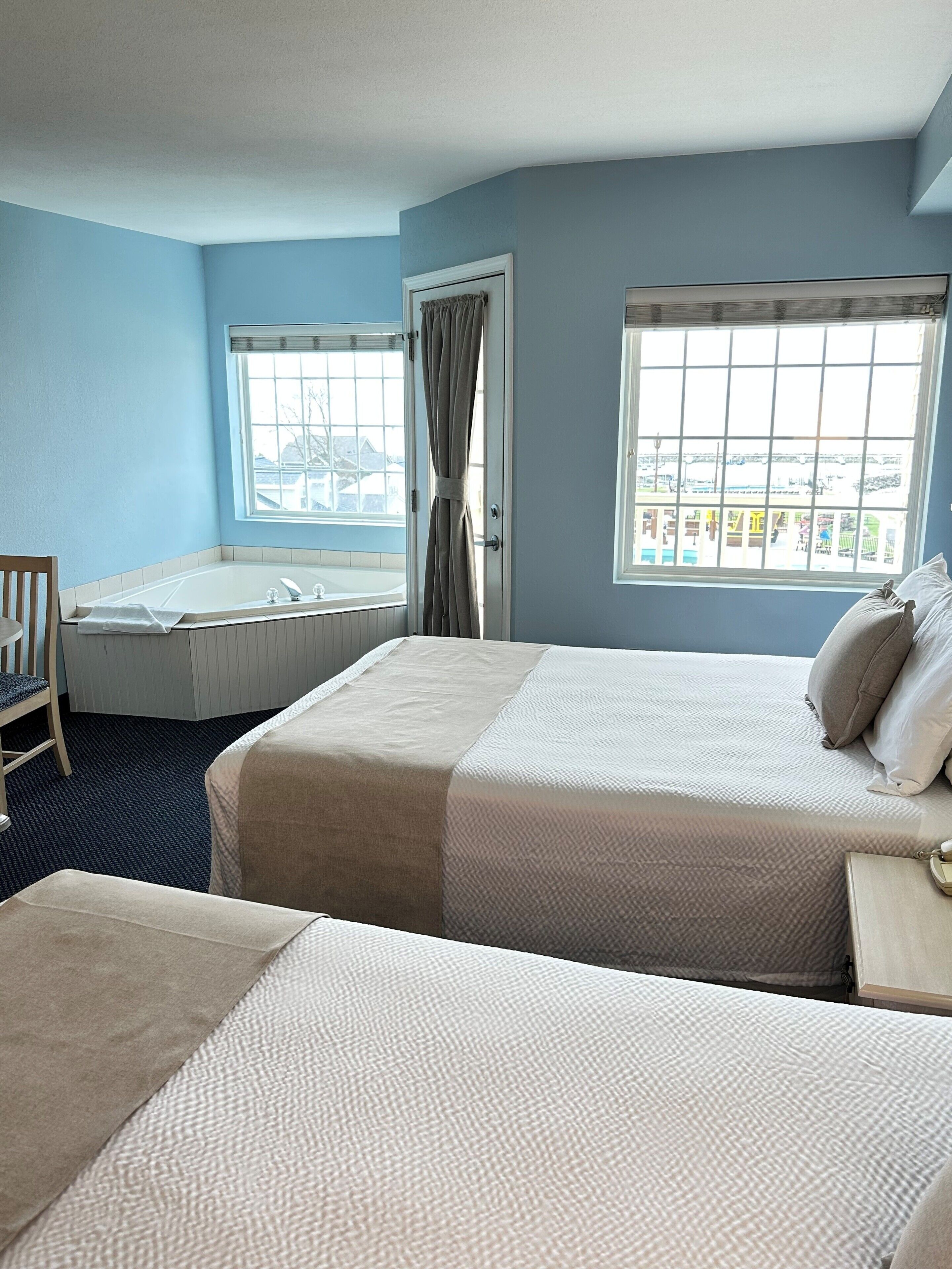 Ein Hotelzimmer mit einem großen Bett, einem Einzelbett, einer Badewanne und einem Fenster mit Blick.