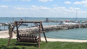 A coastal area with a wooden swing, a grassy area, a rocky breakwater, and boats docked at a pier. - South Beach Resort Hotel (Marblehead)