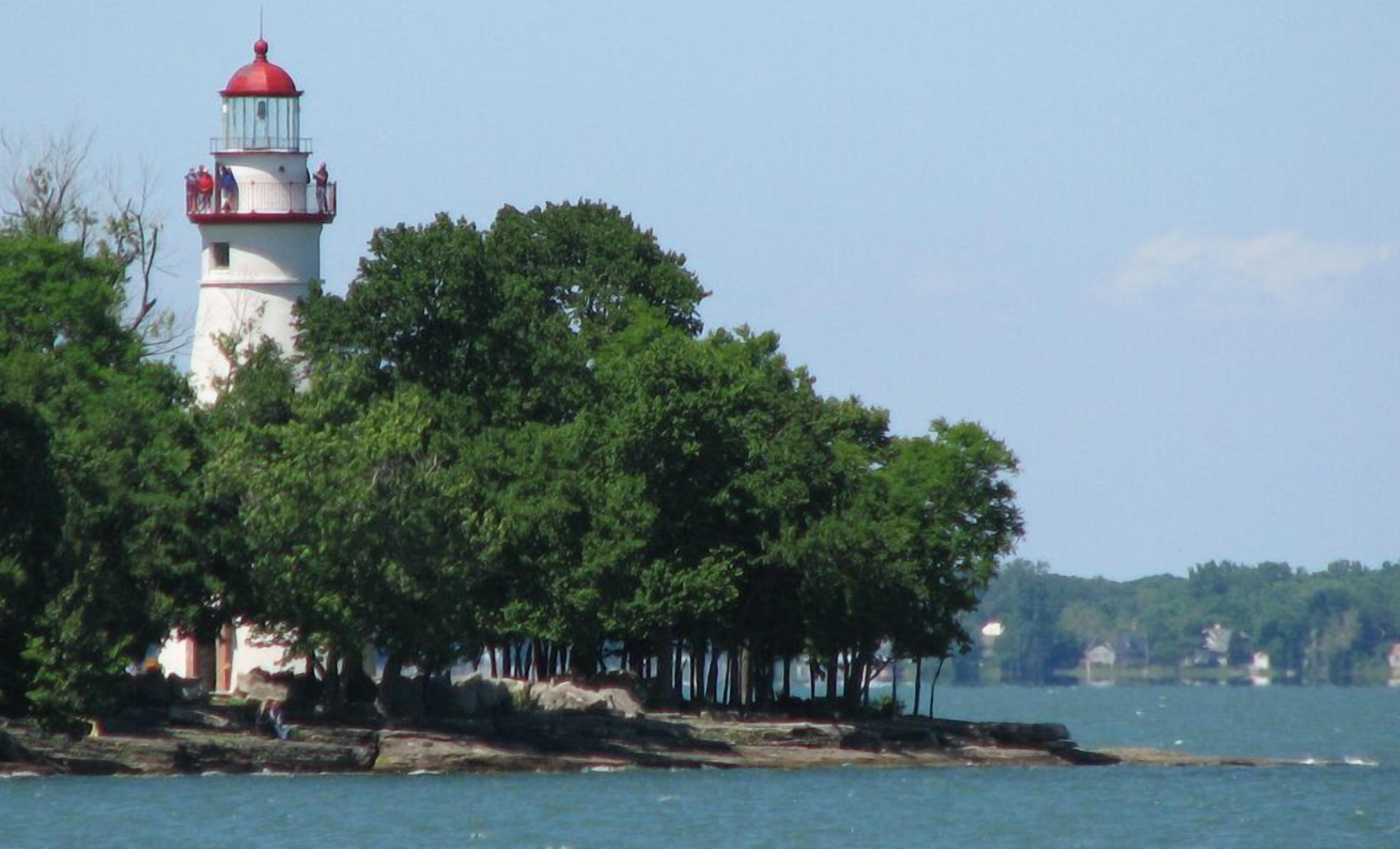 A lighthouse on a rocky island with dense trees.