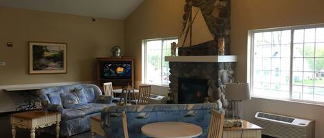A cozy living room with a stone fireplace, a blue sofa, a round table, and a television.