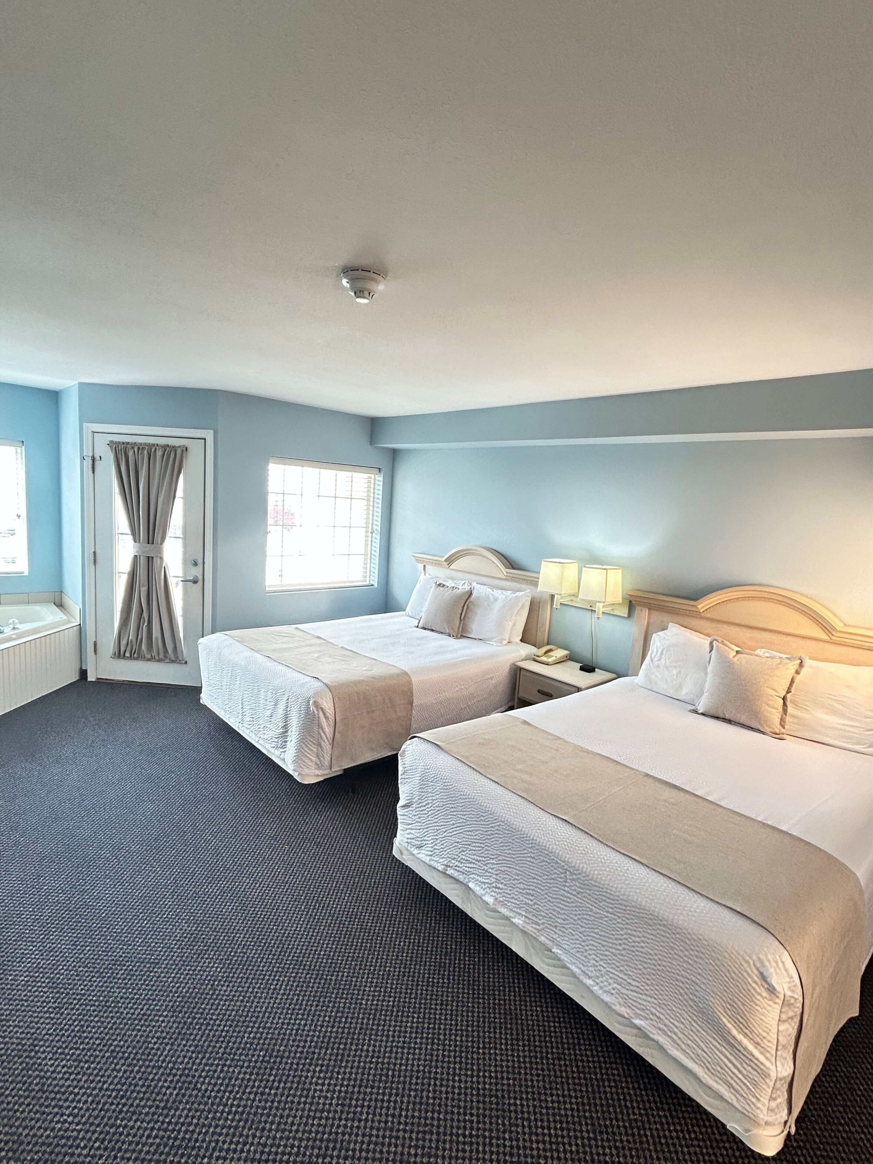 Habitación de hotel con dos camas, un baño y una ventana con cortinas.