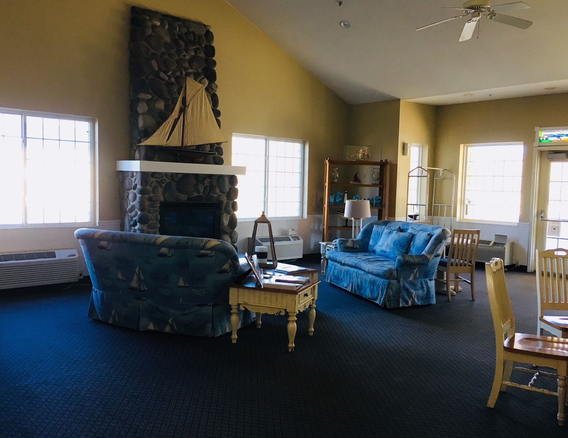 A living room with a stone fireplace, two blue armchairs, a wooden coffee table, and a bookshelf.