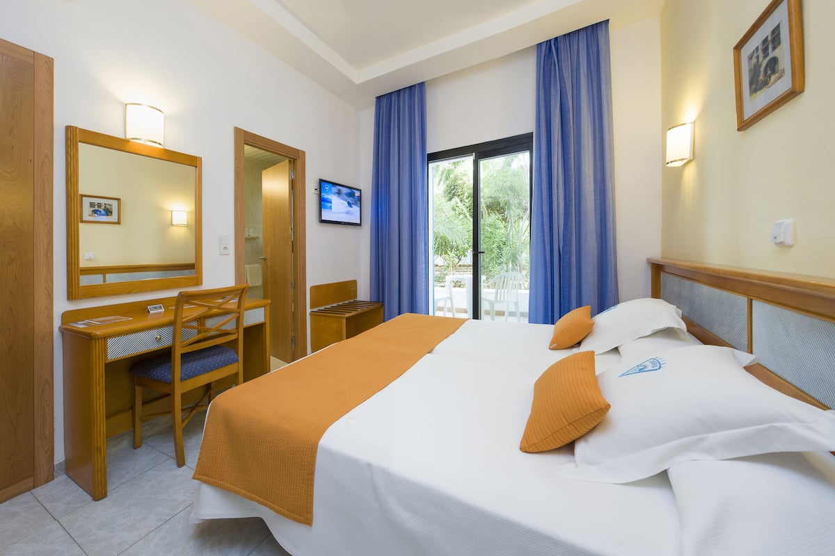 Habitación de hotel con cama, escritorio, silla y vistas a zonas verdes por la ventana.