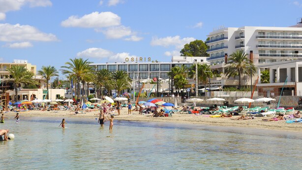 A beach with a hotel named "OSIRIS" in the background, palm trees, and people enjoying the beach. - Hotel Osiris Ibiza (Sant Antoni de Portmany)