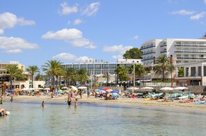 Une plage avec, en arrière-plan, un hôtel appelé « OSIRIS », des palmiers et des personnes qui profitent de la plage.