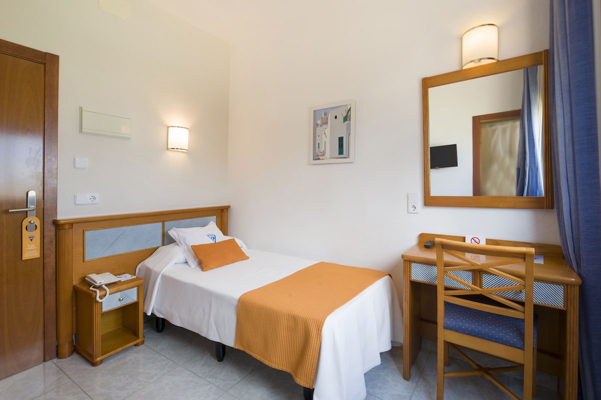 Una habitación de hotel con cama, mesita de noche, silla, escritorio y espejo.
