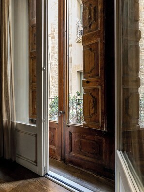 Puerta de madera con un panel de vidrio, que da a un espacio exterior con pared de piedra y un balcón.