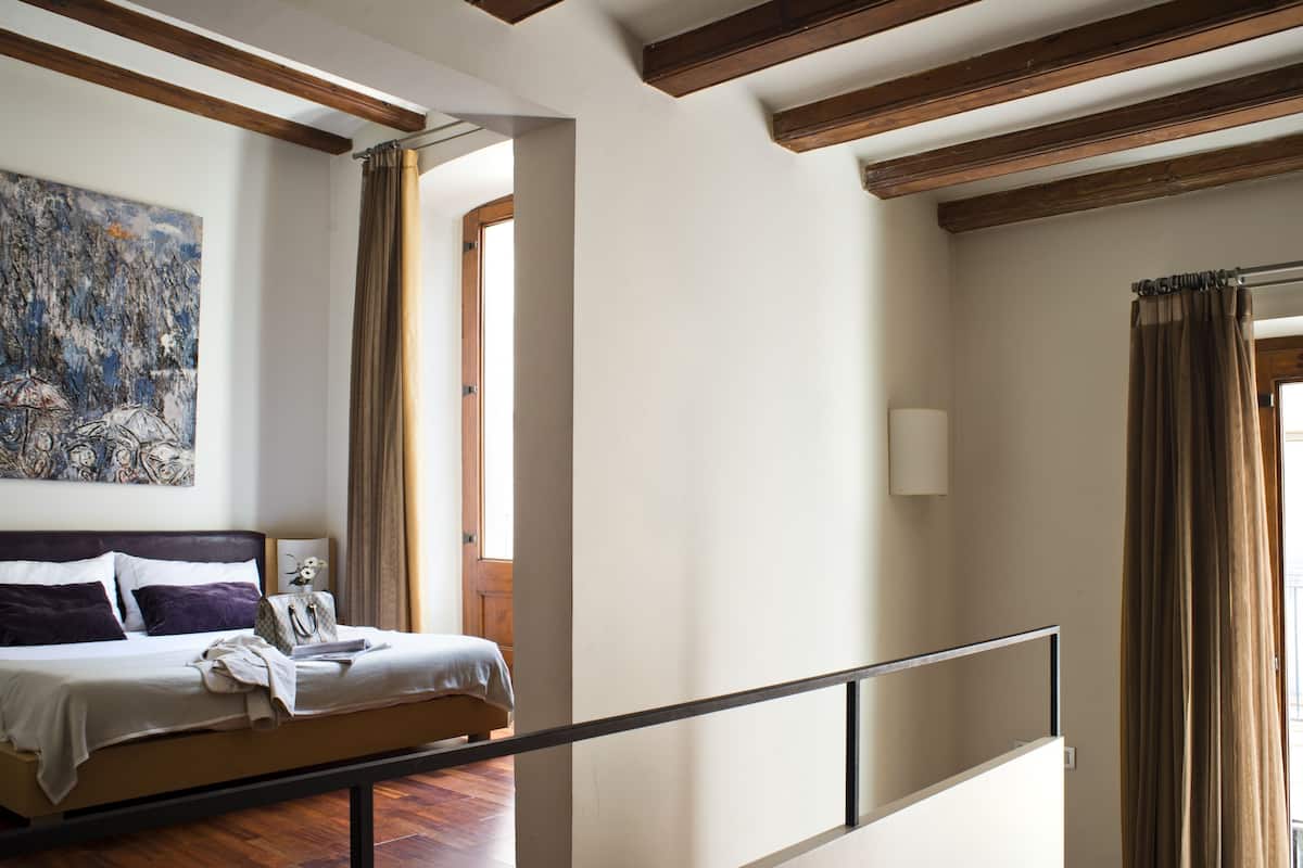 Ein Schlafzimmer mit Bett, Nachttisch, einem Bild an der Wand und einem Fenster mit Vorhängen.