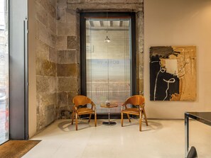 Una habitación con dos sillas de madera, una mesita, una ventana con persianas y un cuadro en la pared.