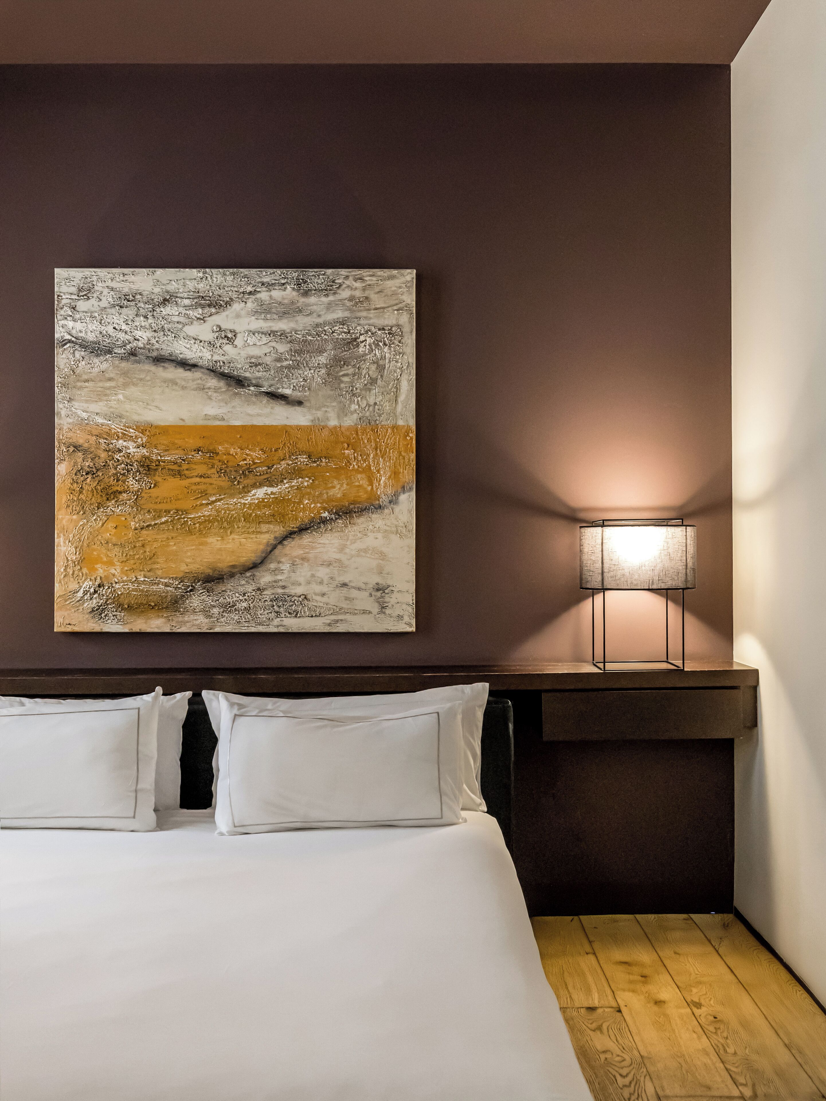 Un dormitorio con un cuadro abstracto grande, una lámpara de noche y una cama bien hecha.