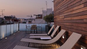 Terraza en la azotea con piso de madera, sillones de descanso y vista panorámica de la ciudad.