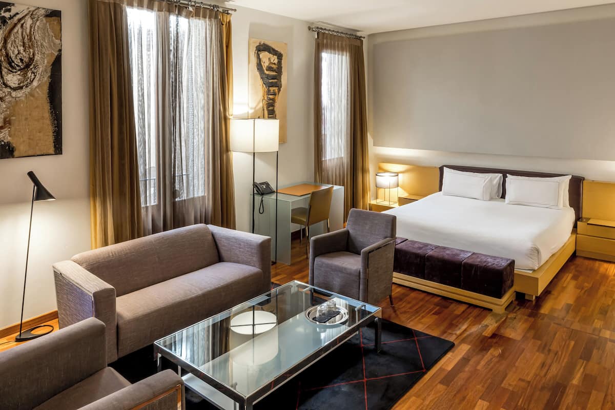 Ein Hotelzimmer mit einem Bett, einer Couch, einem Sessel, einem Glastisch und einem Schreibtisch mit Lampe.