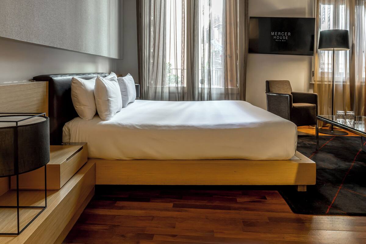 Ein modernes Hotelzimmer mit einem großen Bett, einem an der Wand montierten Fernseher und einer Sitzecke mit Tisch und Stühlen.