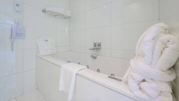 A modern bathroom with a large bathtub, a towel rack with robes, and a wall-mounted air conditioning unit.