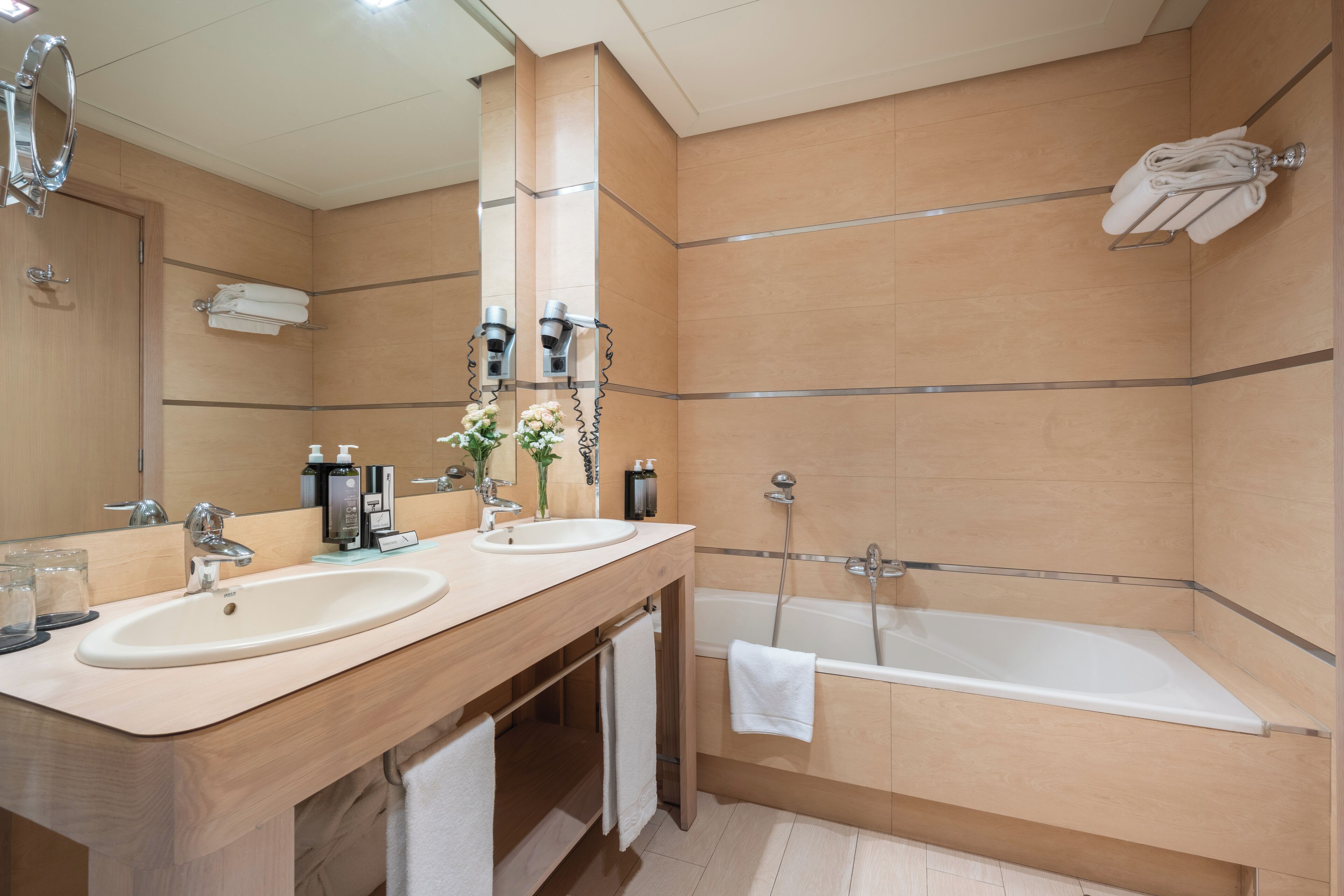 Un baño moderno con dos lavamanos, un espejo grande, una bañera y un perchero para toallas.