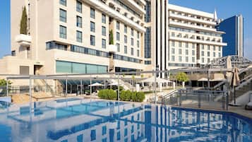 Un hotel moderno con una piscina grande, varios pisos y un cielo azul despejado.