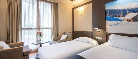 Habitación de hotel con dos camas, una silla, una mesita con un florero y un ventanal con cortinas.