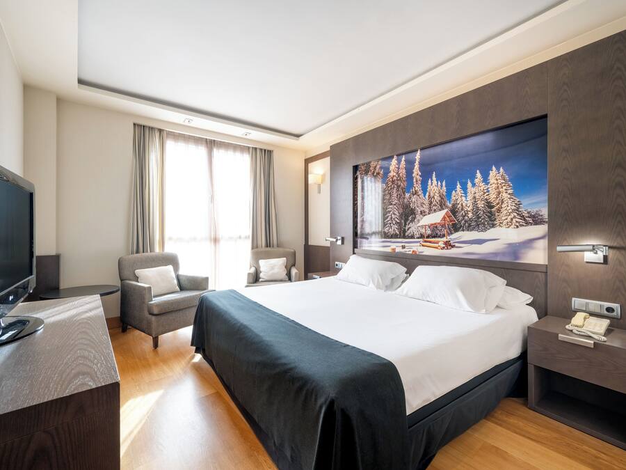 Una habitación de hotel moderna con una cama grande, un televisor, un escritorio y un cuadro de un paisaje nevado.