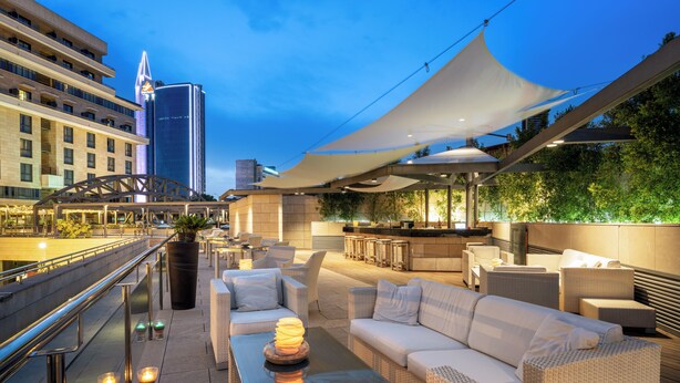 Un bar situé sur un toit, avec une terrasse, une vue sur les toits de la ville et une architecture moderne.