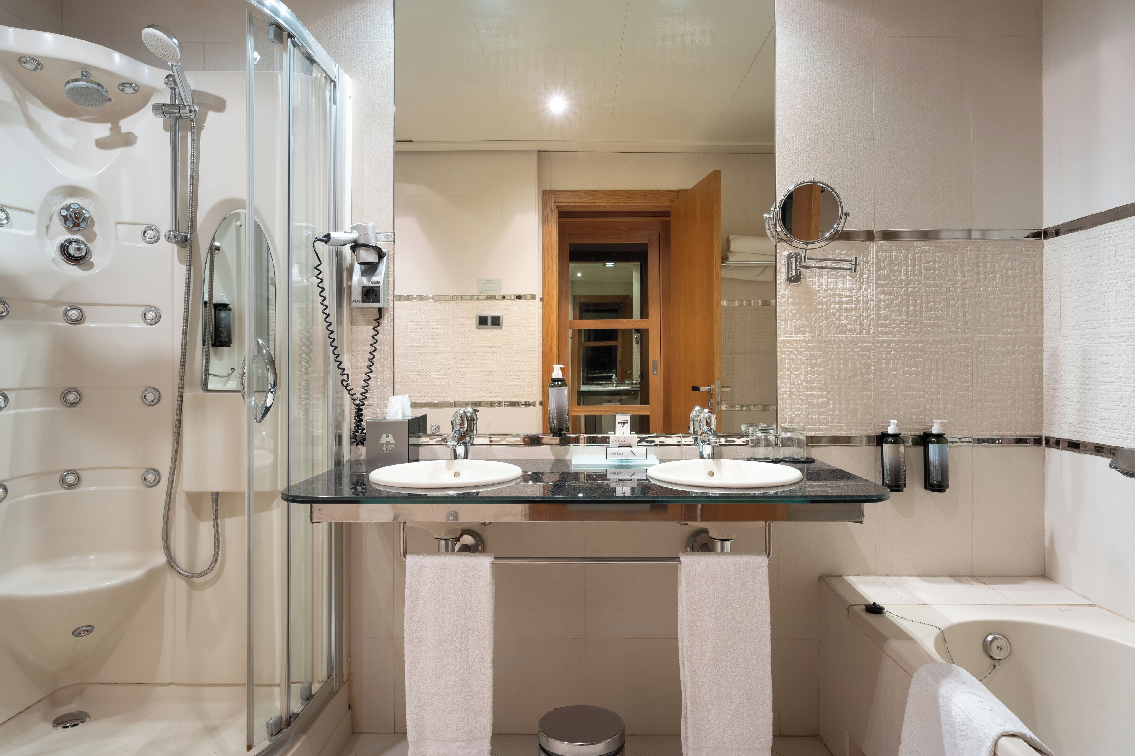 A modern bathroom with a glass-enclosed shower, two sinks, a bathtub, and a mirror.