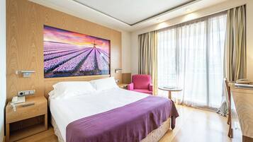 Habitación de hotel con una cama grande, un escritorio, una silla, una mesita y un cuadro de un campo.