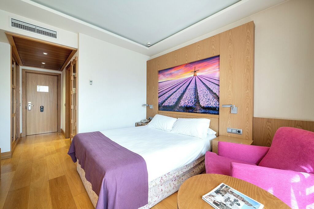 Ein Hotelzimmer mit einem Bett, einem rosa Sessel, einem runden Tisch und einem Bild an der Wand.