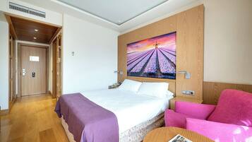 Ein Hotelzimmer mit einem Bett, einem rosa Sessel, einem runden Tisch und einem Bild an der Wand.