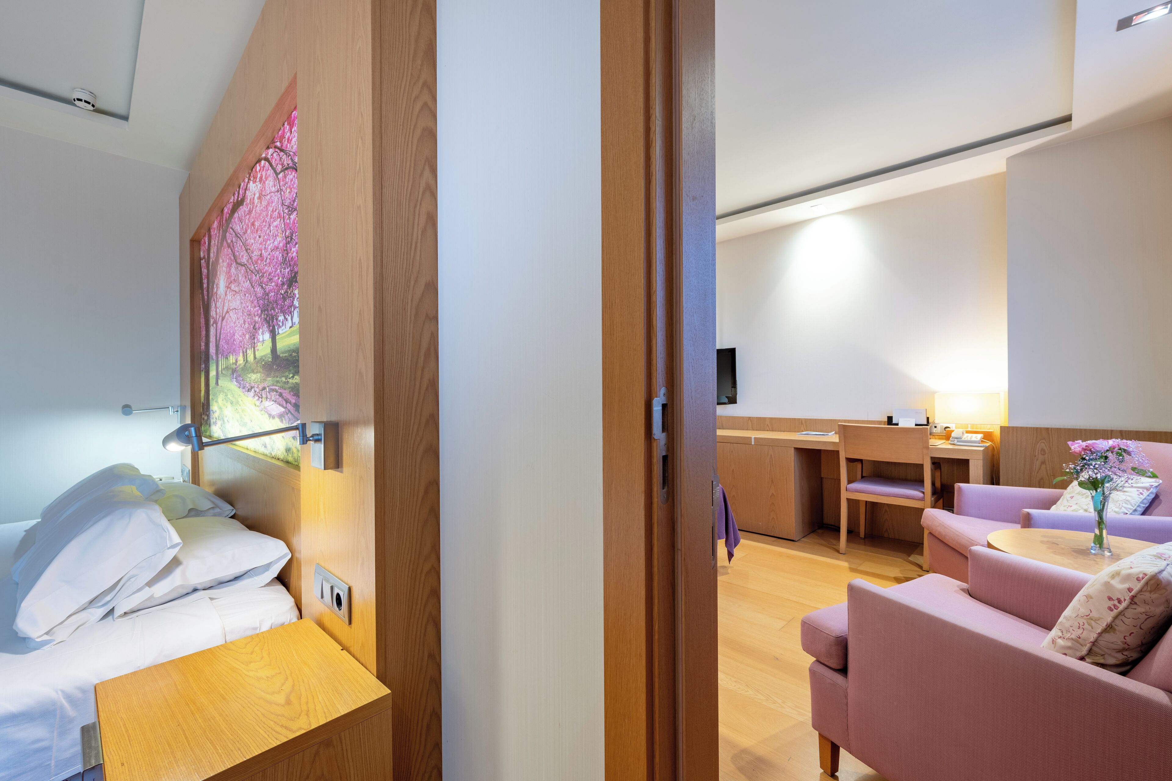 A modern hotel room with a bed, a desk, a sofa, and a small table.