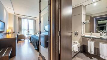 Habitación de hotel con cama, mesita de noche, televisor y baño que incluye espejo, lavabo y toallero.