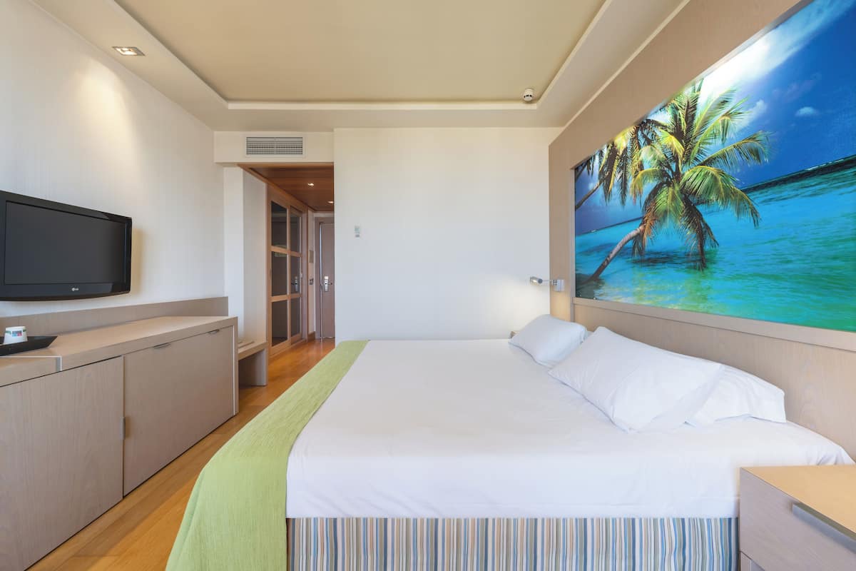Quarto com cama, televisão, quadro de uma praia e guarda-roupa.