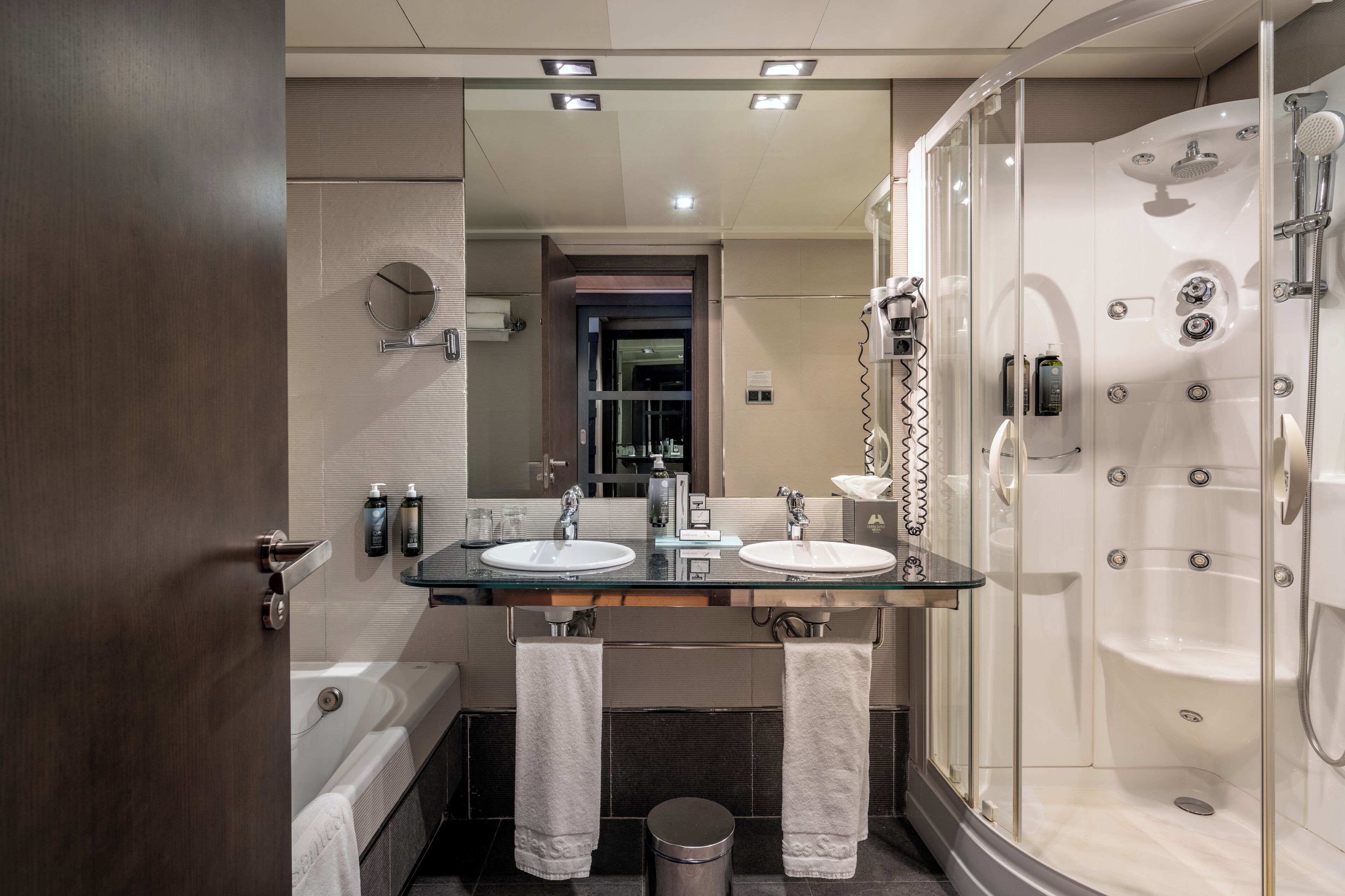 Une salle de bain moderne avec deux lavabos, un grand miroir, une baignoire et une douche séparée par une paroi de verre.