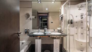 Une salle de bain moderne avec deux lavabos, un grand miroir, une baignoire et une douche séparée par une paroi de verre.