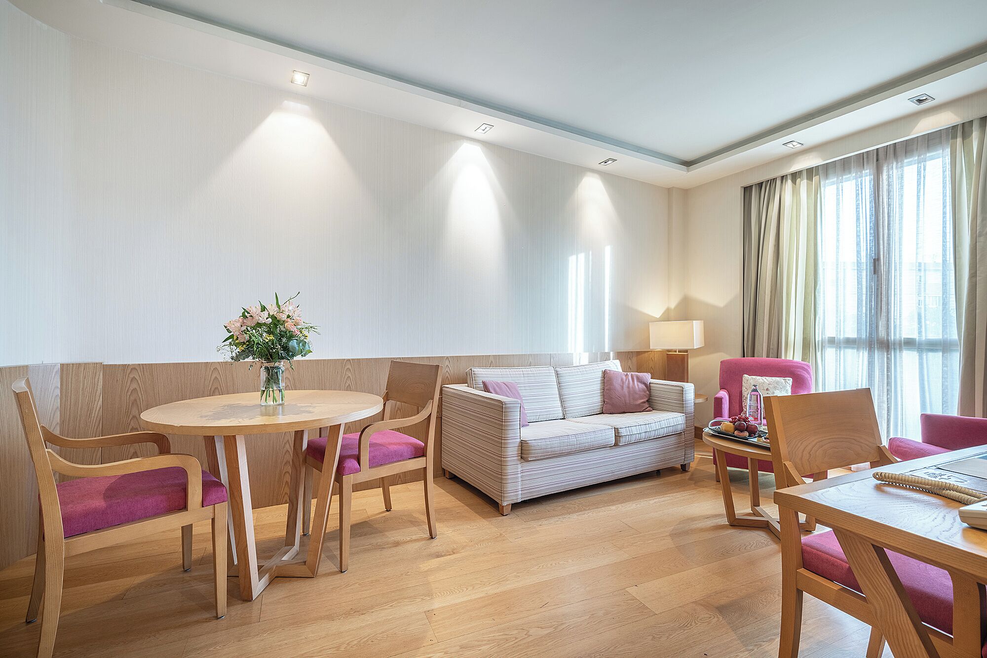 A modern living room with a round wooden table, two sofas, and a pink armchair.