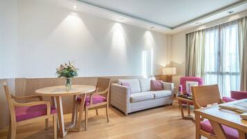Una sala de estar moderna con una mesa redonda de madera, dos sofás y un sillón rosa.