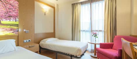 A hotel room with two beds, a red armchair, a small table, and a painting of a cherry blossom tree.