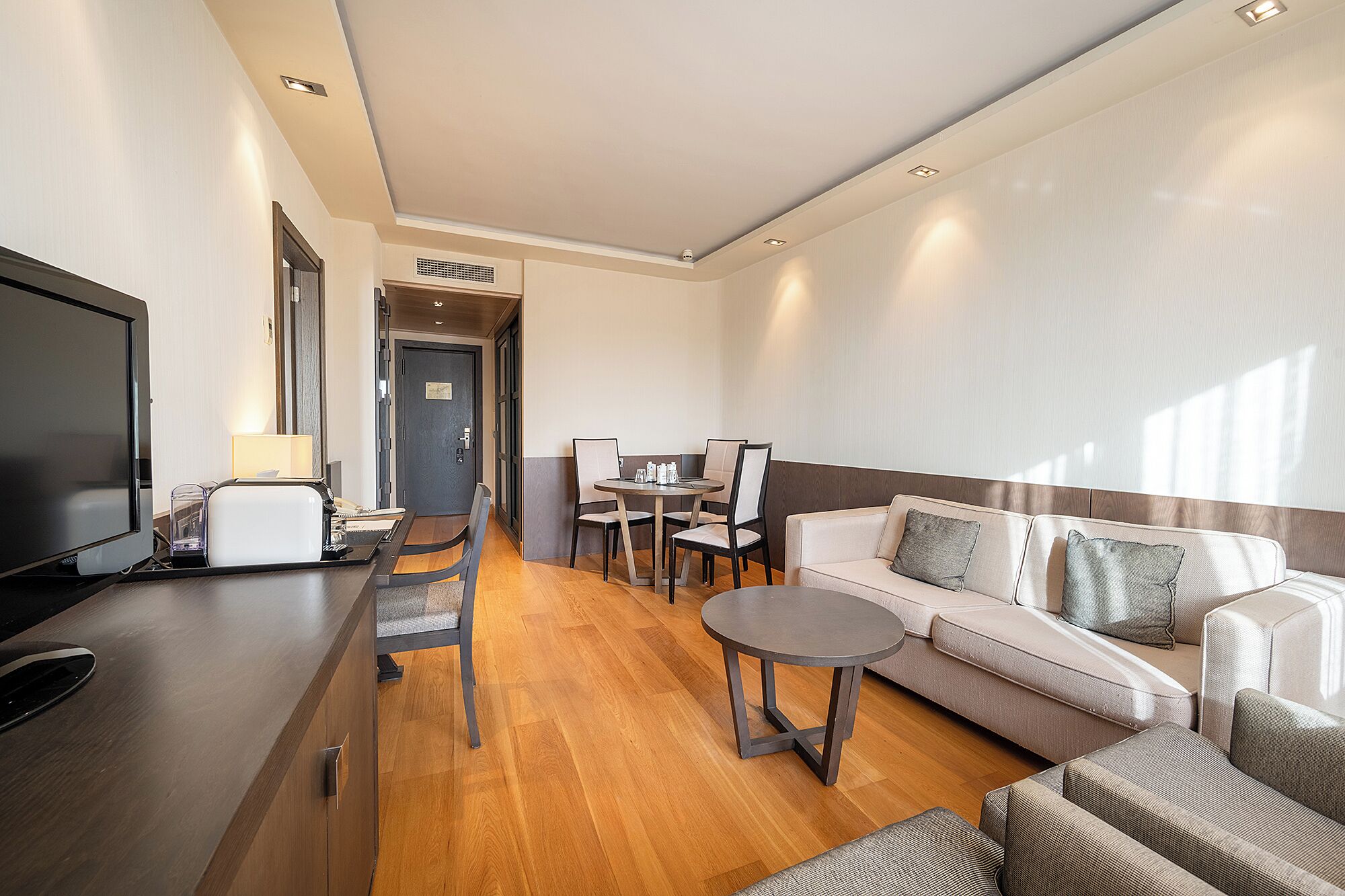 Une chambre d’hôtel moderne équipée d’un téléviseur à écran plat, d’une table à manger avec des chaises, d’un canapé et d’une petite table basse.